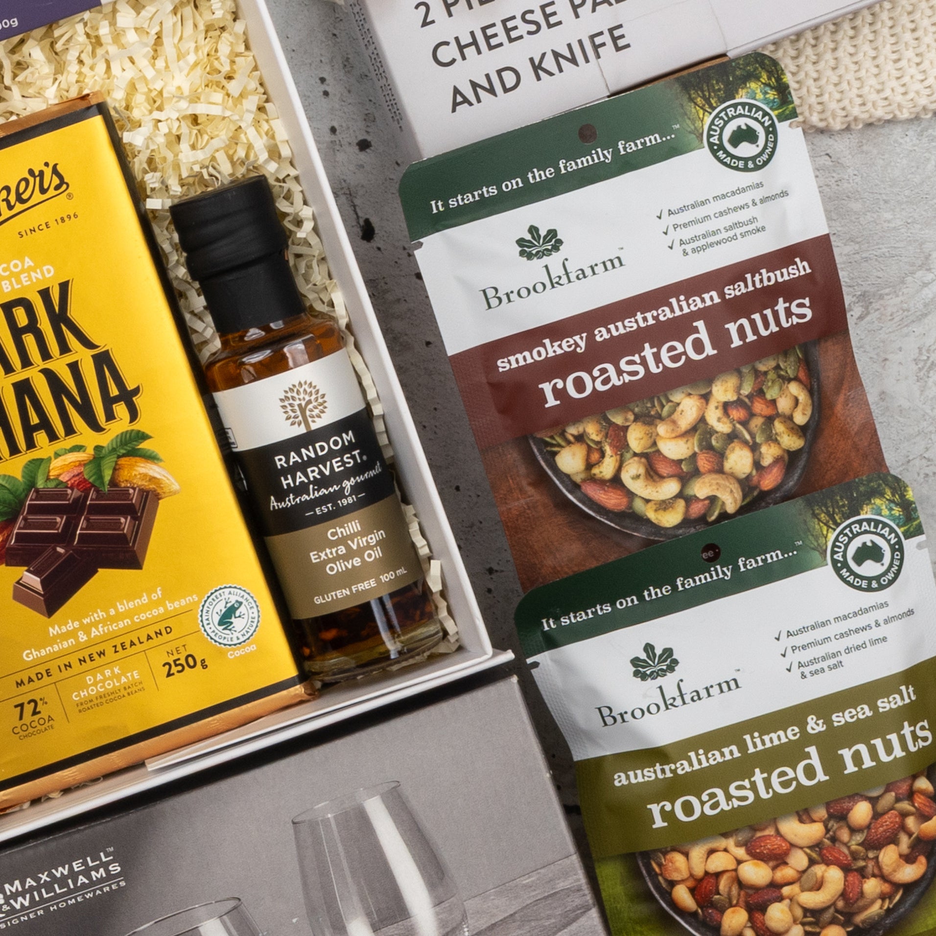 A close-up of The Hamper Boutique Co’s Moët & Chandon Rosé Grand Celebration Hamper featuring a bottle of rosé, gourmet dark chocolate, Brookfarm roasted Australian nuts, and two stemless wine glasses on shredded paper filling.