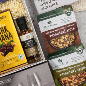 A close-up of The Hamper Boutique Co’s Moët & Chandon Rosé Grand Celebration Hamper featuring a bottle of rosé, gourmet dark chocolate, Brookfarm roasted Australian nuts, and two stemless wine glasses on shredded paper filling.