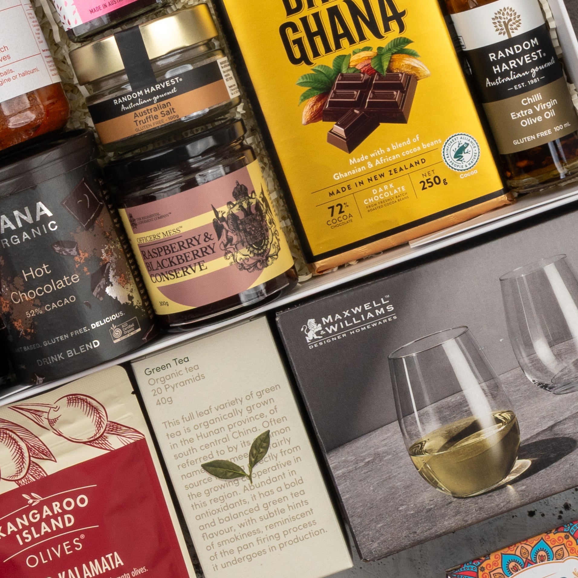A close-up of The Hamper Boutique Co's Moët & Chandon Rosé Grand Celebration Hamper shows gourmet preserves, chocolate, tea, and a box with two stemless wine glasses, all beautifully arranged with elegantly designed labels.