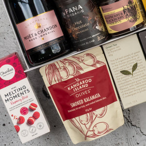 The Hamper Boutique Co's Moët & Chandon Rosé Grand Celebration Hamper features champagne, Pana Organic hot chocolate, berry conserve, smoked Kalamata olives, Love Tea, and Charlie’s mini raspberry bliss biscuits.