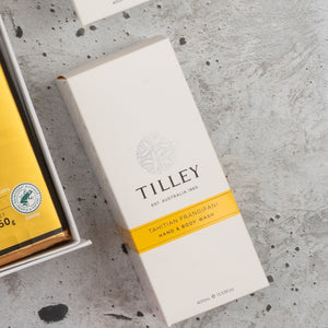 A rectangular white box labeled “Veuve Clicquot Grand Celebration Hamper” by The Hamper Boutique Co lies on a gray surface next to another box with gold and green packaging.