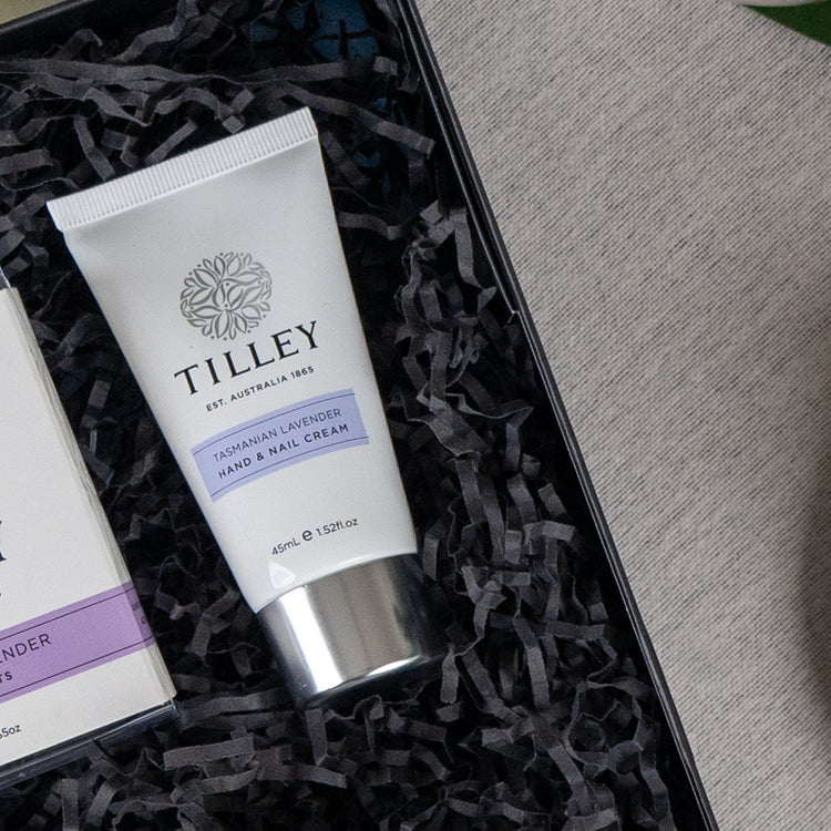 A Self-Care and Relaxation Hamper by The Hamper Boutique Co sits on a grey fabric surface, featuring a gift box filled with black shredded paper and a matching box.