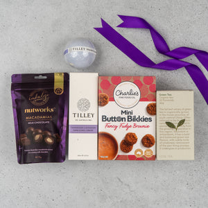 The Hamper Boutique Co's Tea Lover's Essentials Hamper features milk chocolate macadamias, Tilley Tasmanian lavender hand cream, a bath bomb, Charlies Mini Button Bikkies, a green tea card, and is finished with a purple ribbon.