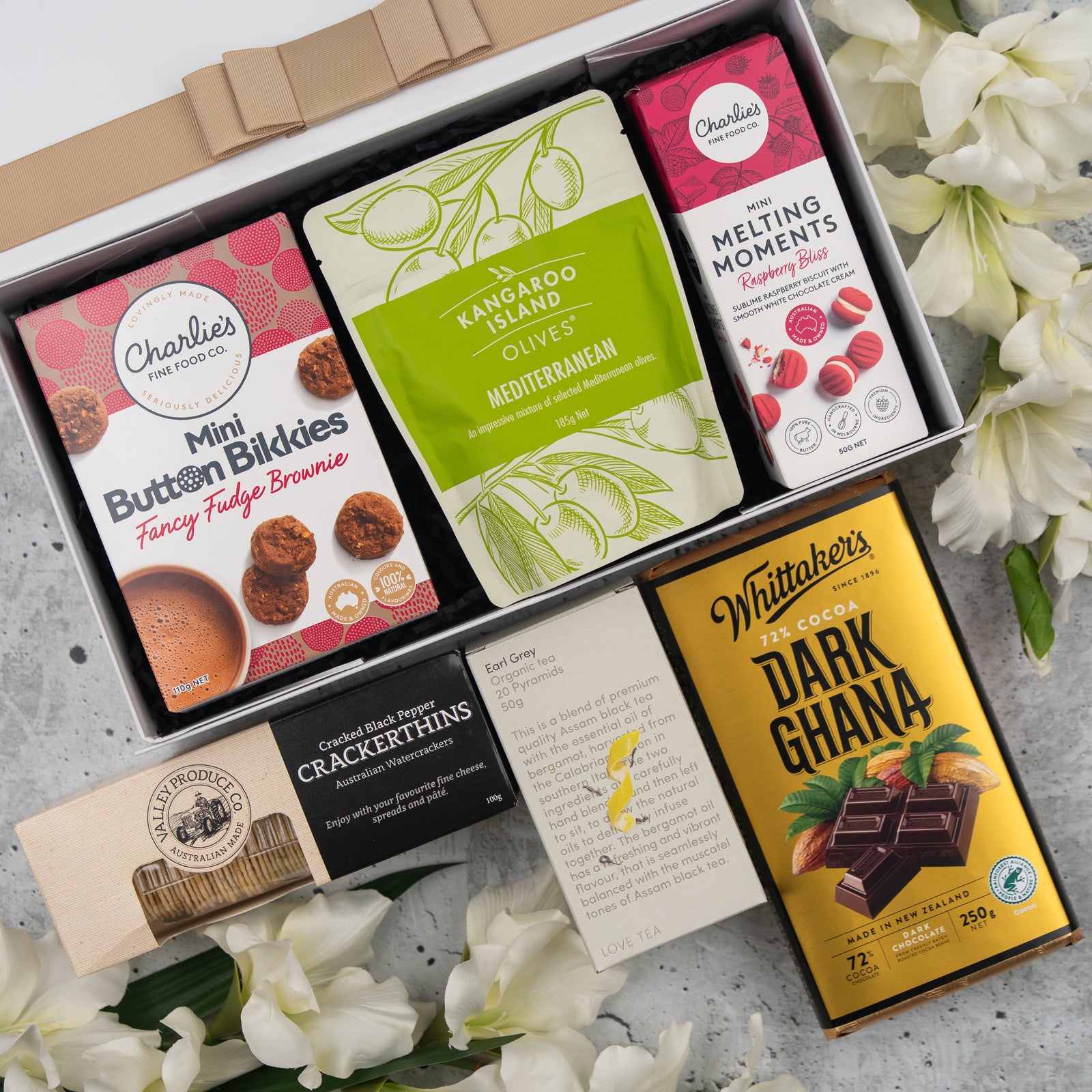 The Hamper Boutique Co's Black Tea Haven Hamper features fudge brownie bites, Mediterranean olives, raspberry melting moments, seeded crackers, dark Ghana chocolate, a note card—all beautifully boxed and accented with white flowers.