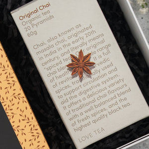 The Exotic Explorations Tea Hamper by The Hamper Boutique Co features 20 pyramids of organic chai tea, blending traditional spices with black tea, and includes details on chai’s origins and benefits. The box is adorned with a star anise design.