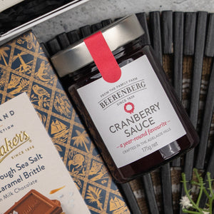 An Exotic Explorations Tea Hamper by The Hamper Boutique Co is displayed on a dark patterned surface, with some white flowers in the corner.