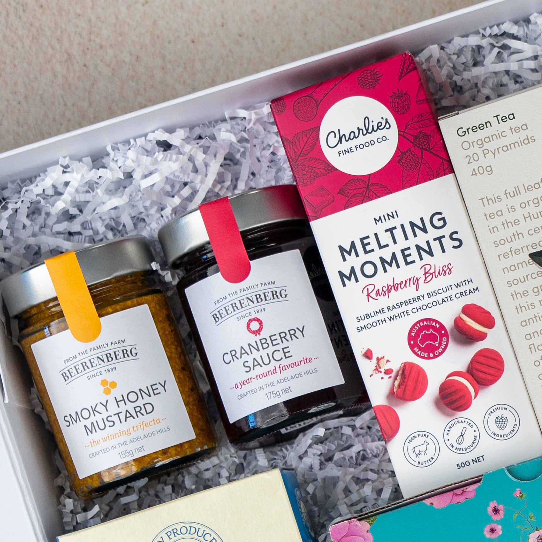 The Hamper Boutique Co Sweet Indulgence Tea Hamper features Beerenberg Smoky Honey Mustard, Beerenberg Cranberry Sauce, and Charlies Raspberry Bliss Melting Moments, beautifully presented on white shredded paper.