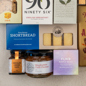 The Hamper Boutique Co's Ultimate Tea Indulgence Hamper features gourmet tea, shortbread, chocolate liqueur sauce, chutney, and a FLWR Purple Reign soap box—all beautifully arranged for a luxurious treat.