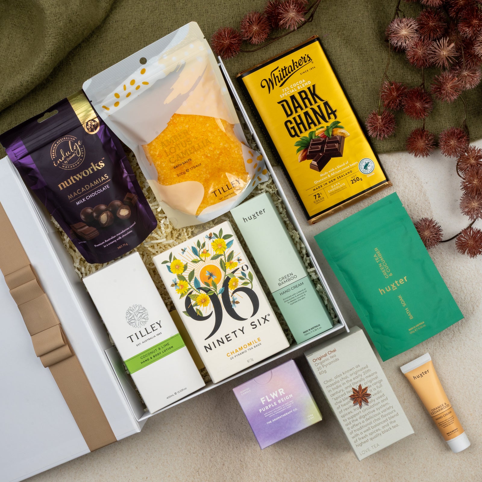 The Hamper Boutique Co’s Wellness Home Entertaining Hamper features chocolate, tea, macadamias, soap, body lotion, hand cream, and a green face mask sachet—beautifully arranged on a soft cream background.