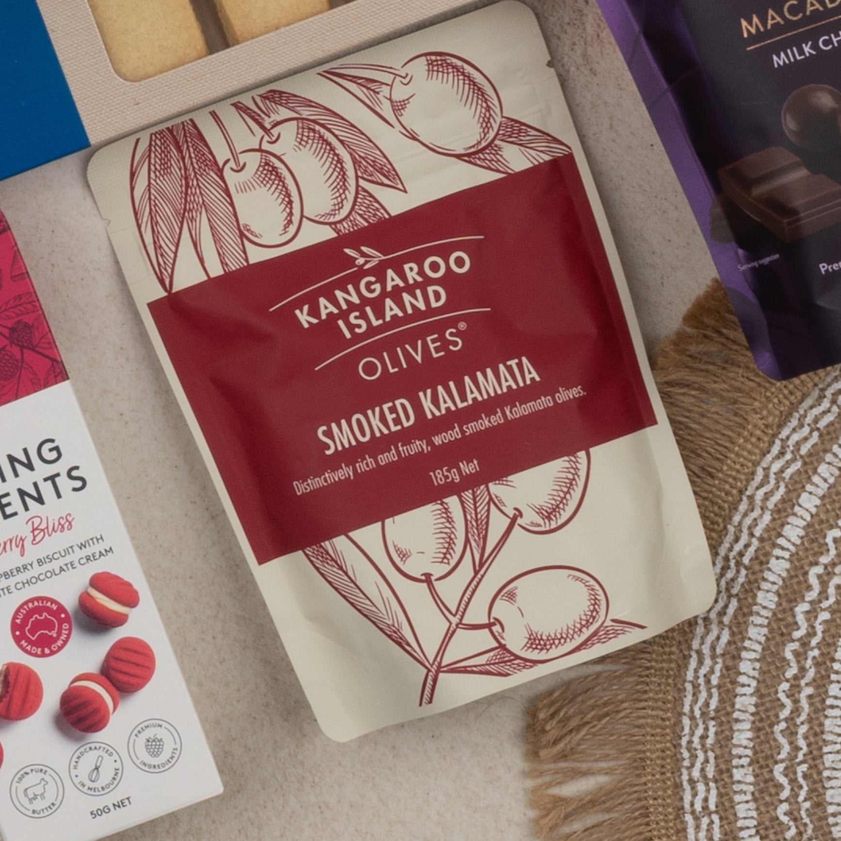 A close-up of The Hamper Boutique Co Tea Time Gourmet Hamper surrounded by assorted snack packaging on a neutral background.