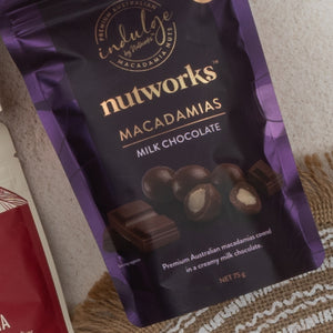 A Tea Time Gourmet Hamper by The Hamper Boutique Co rests on a woven mat. The package displays gourmet treats, with elegant gold and white text highlighting this Australian product.
