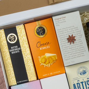 The Hamper Boutique Co’s Premium Tea Experience Hamper features three boxes of gourmet treats—butter shortbread biscuits, cheese nibbles, and organic chai tea—beautifully presented in a gift box.