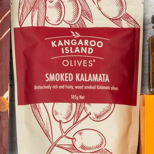 A 185g red and cream packet of Smoked Kalamata Olives from The Hamper Boutique Co’s Gourmet Getaway Gift Hamper, featuring an illustrated olive branch and described as distinctively rich, fruity, and wood smoked.