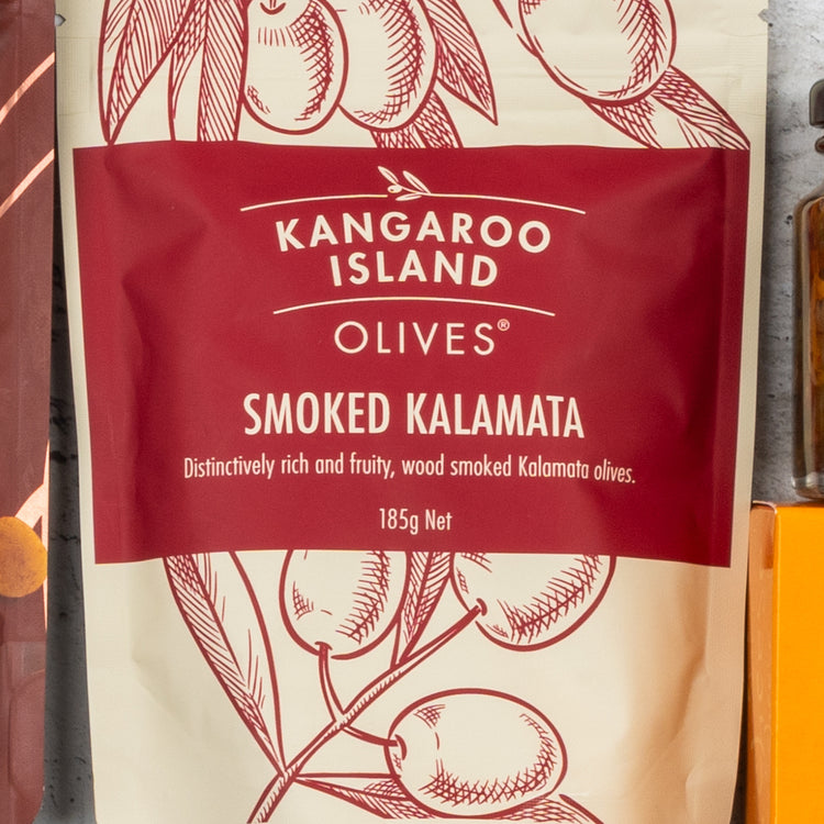 A 185g red and cream packet of Smoked Kalamata Olives from The Hamper Boutique Co’s Gourmet Getaway Gift Hamper, featuring an illustrated olive branch and described as distinctively rich, fruity, and wood smoked.