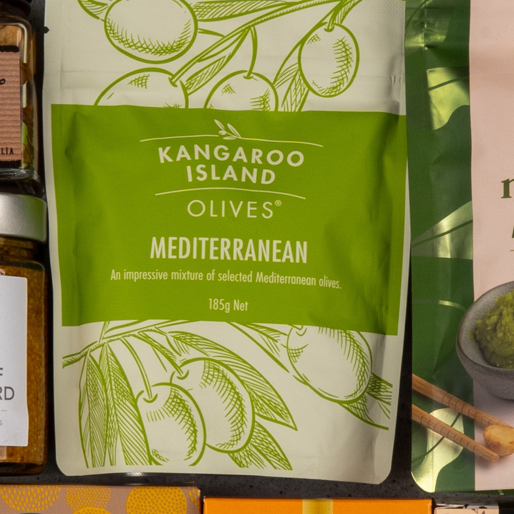 A package labeled The Hamper Boutique Co Gourmet Delights Hamper with an illustration of olive branches states it contains an impressive mixture of selected Mediterranean olives, 185 grams.