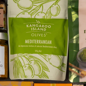 A package labeled The Hamper Boutique Co Gourmet Delights Hamper with an illustration of olive branches states it contains an impressive mixture of selected Mediterranean olives, 185 grams.