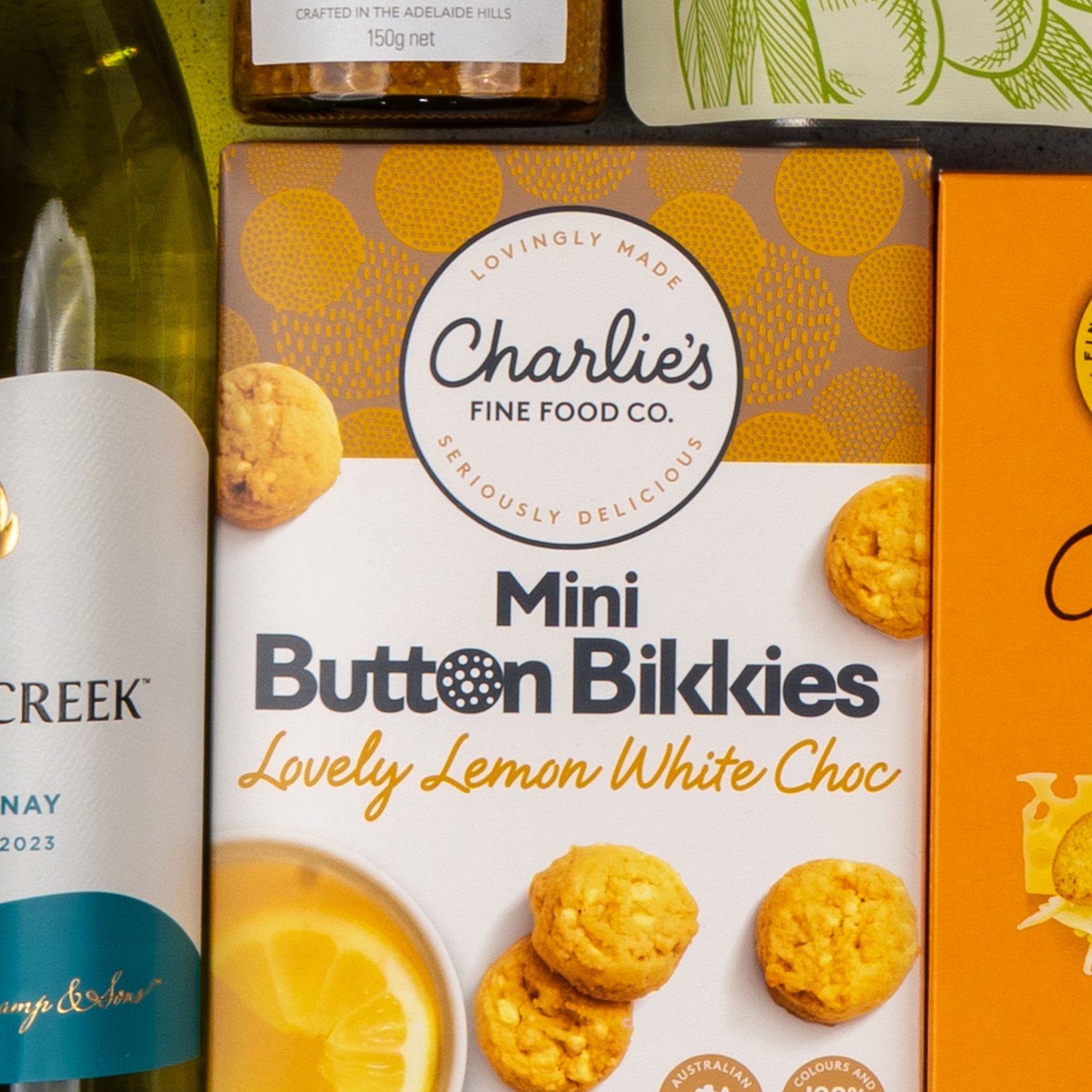 A close-up of The Hamper Boutique Co’s Gourmet Delights Hamper, featuring a yellow box of mini cookies with lemon slices, displayed alongside a wine bottle and other gourmet treats.