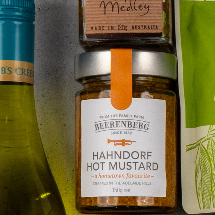 A close-up of items from The Hamper Boutique Co’s Gourmet Delights Hamper, featuring a green wine bottle, Beerenberg Hahndorf Hot Mustard, medley preserve, and part of a green and white packaged item.