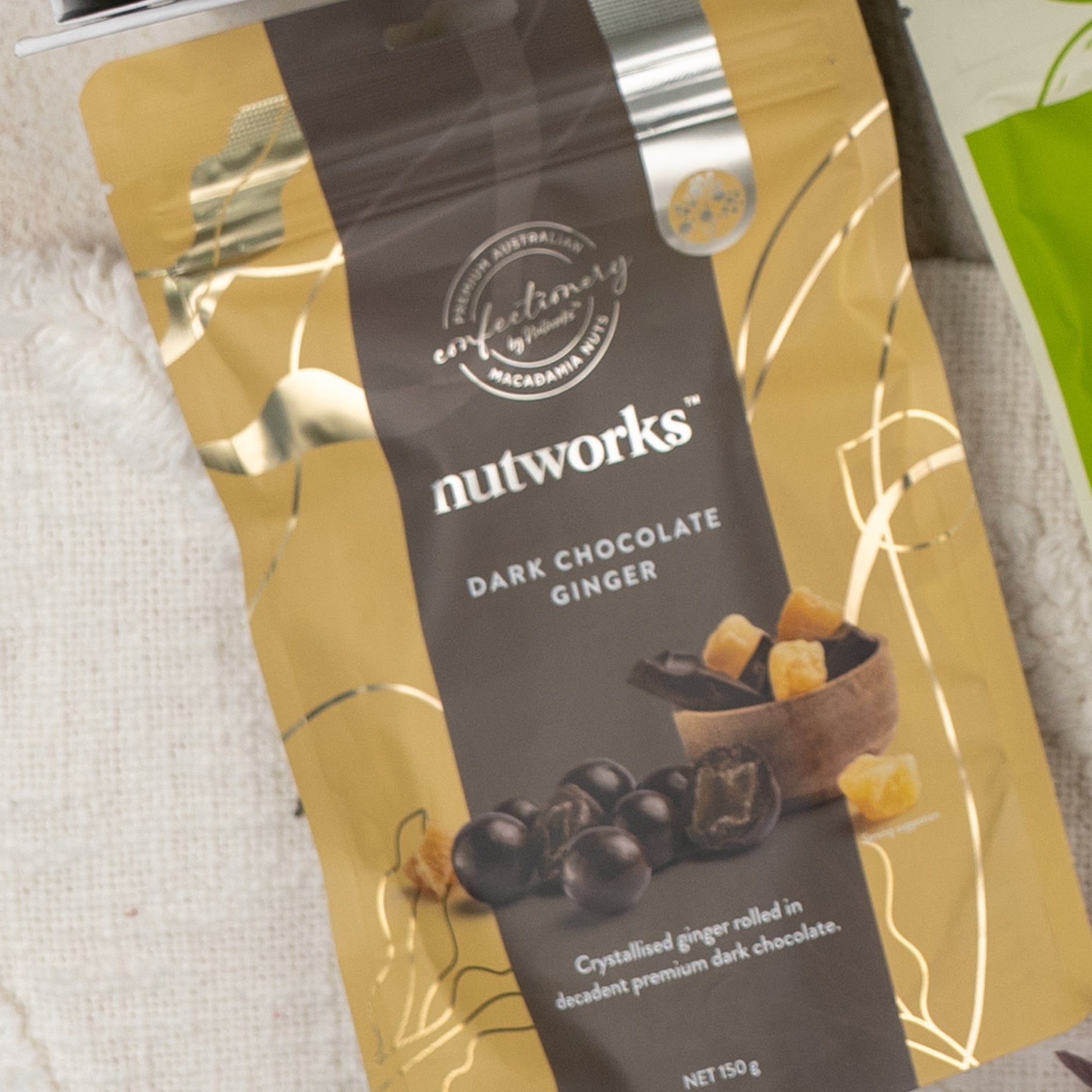 A Gourmet Indulgence Hamper from The Hamper Boutique Co, in gold and dark brown packaging with white text, features an image of chocolate-coated ginger pieces and diced ginger in a bowl on the front.