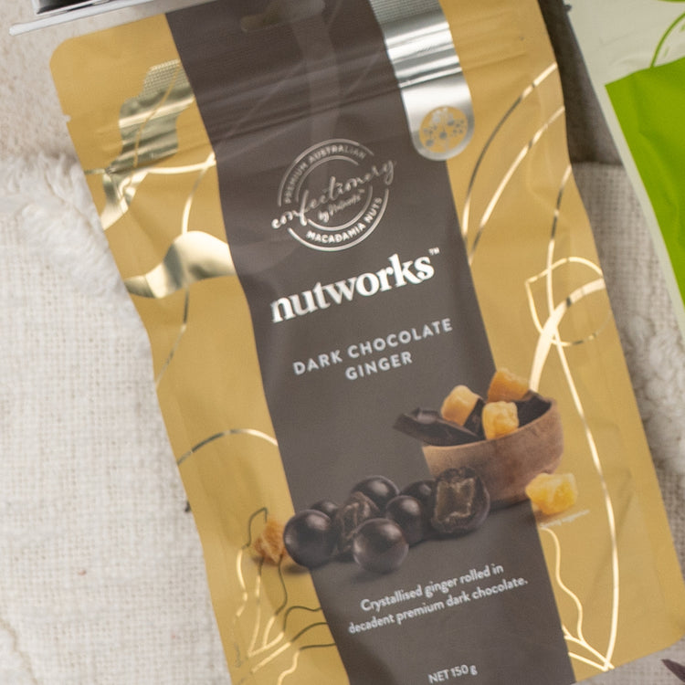 A Gourmet Indulgence Hamper from The Hamper Boutique Co, in gold and dark brown packaging with white text, features an image of chocolate-coated ginger pieces and diced ginger in a bowl on the front.