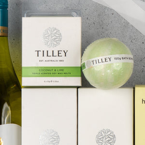 A close-up of The Hamper Boutique Co's "White Wine and Self-Care" set, featuring Coconut & Lime wax melts and a green bath bomb, displayed with a wine bottle on a light gray surface.