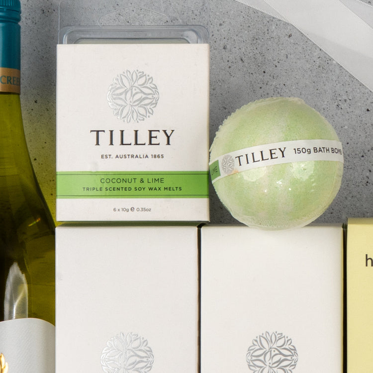 A close-up of The Hamper Boutique Co's "White Wine and Self-Care" set, featuring Coconut & Lime wax melts and a green bath bomb, displayed with a wine bottle on a light gray surface.