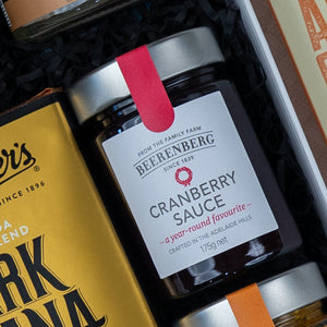 A close-up of a jar inside The Hamper Boutique Co's Gourmet Experience Hamper, showcasing cranberry sauce with a red seal nestled among other gourmet foods.