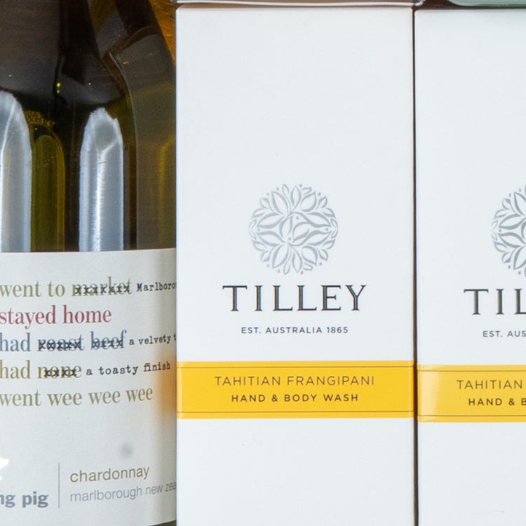 Close-up of the Chardonnay and Self-Care Hamper by The Hamper Boutique Co, featuring two Tilley Tahitian Frangipani hand and body wash bottles beside partially visible wine bottles labeled chardonnay and Marlborough.