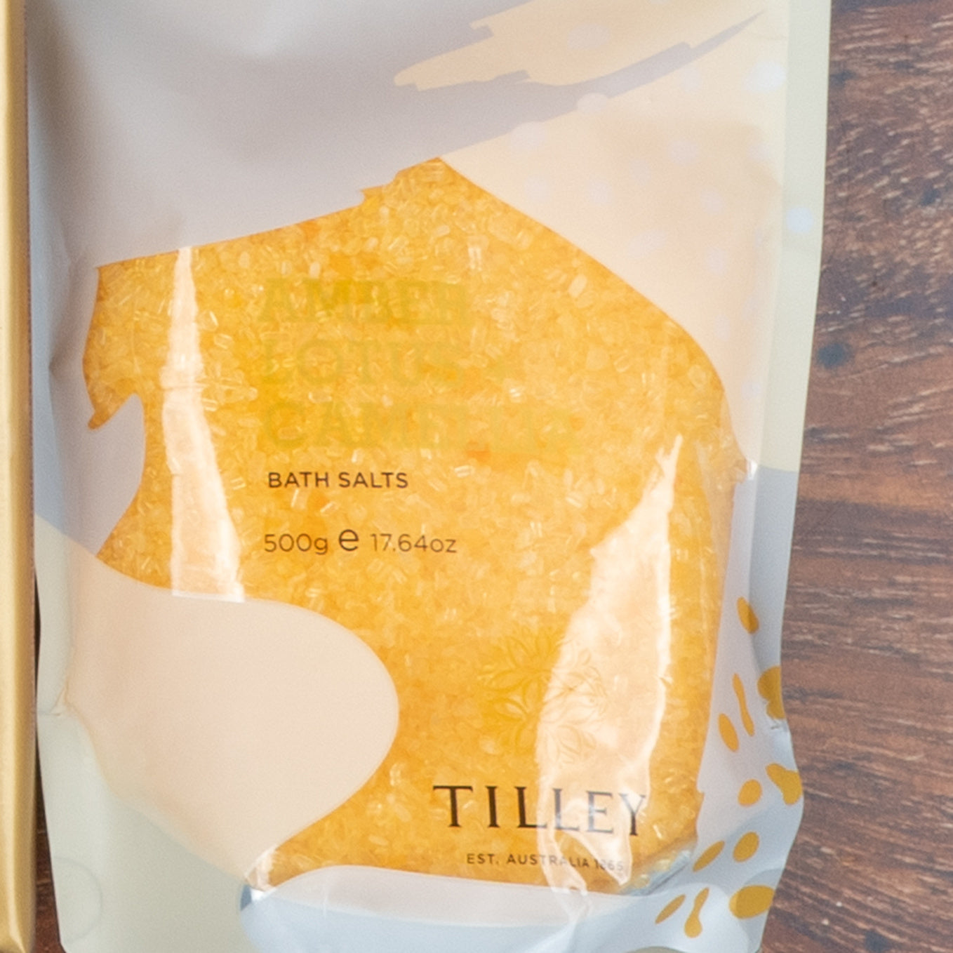 A clear plastic pouch of yellow bath salts from The Hamper Boutique Co’s “Chardonnay and Self-Care Hamper” sits on a wooden surface.