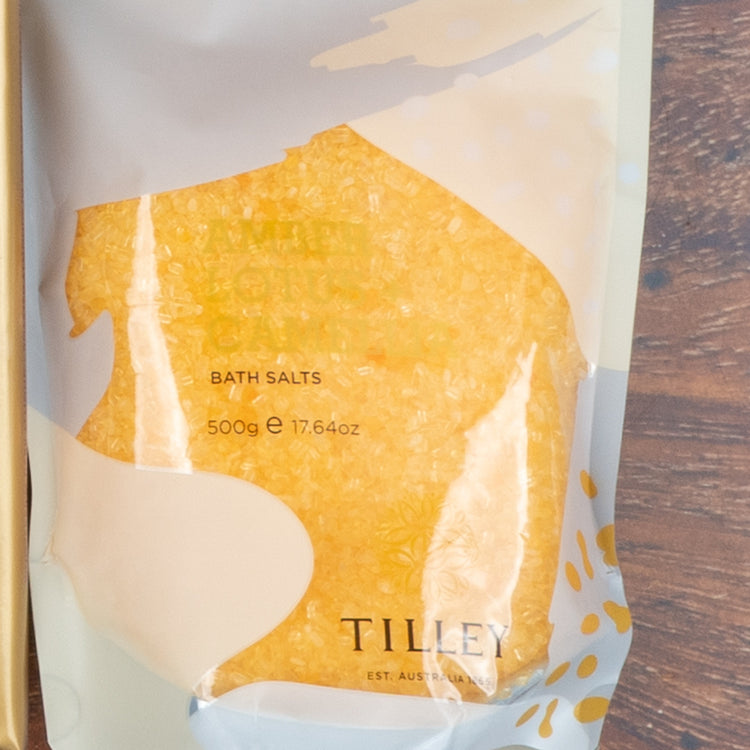 A clear plastic pouch of yellow bath salts from The Hamper Boutique Co’s “Chardonnay and Self-Care Hamper” sits on a wooden surface.