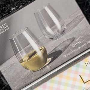 The Hamper Boutique Co Chardonnay and Relaxation Gift Hamper features two 500 ml stemless glasses—one filled with white wine, one empty—displayed on a textured gray background.