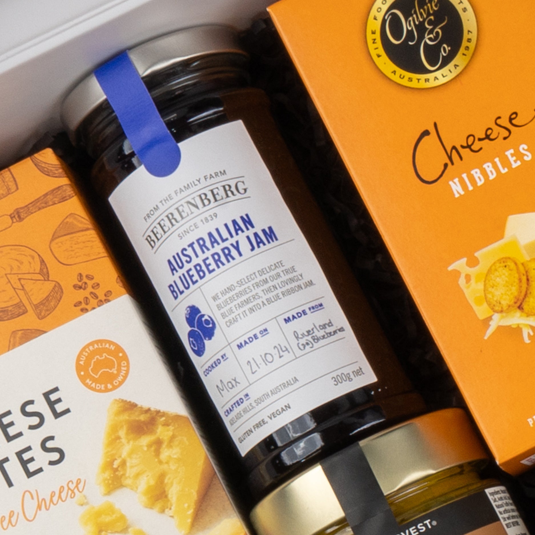 Close-up of The Hamper Boutique Co Gourmet Collection Gift Hamper featuring Beerenberg Australian Blueberry Jam and two orange boxes of cheese snacks, labeled Cheese Bites and Cheese Nibbles, neatly arranged in a gift box.