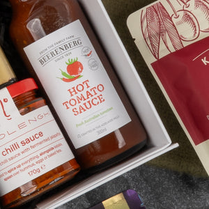 Close-up of The Hamper Boutique Co's Gourmet Collection Gift Hamper, featuring Beerenberg hot tomato sauce and a chili-labeled jar beside a red and cream package, all neatly arranged in the box.