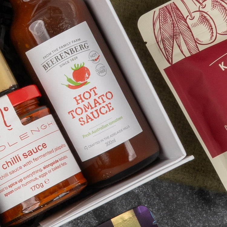 Close-up of The Hamper Boutique Co's Gourmet Collection Gift Hamper, featuring Beerenberg hot tomato sauce and a chili-labeled jar beside a red and cream package, all neatly arranged in the box.