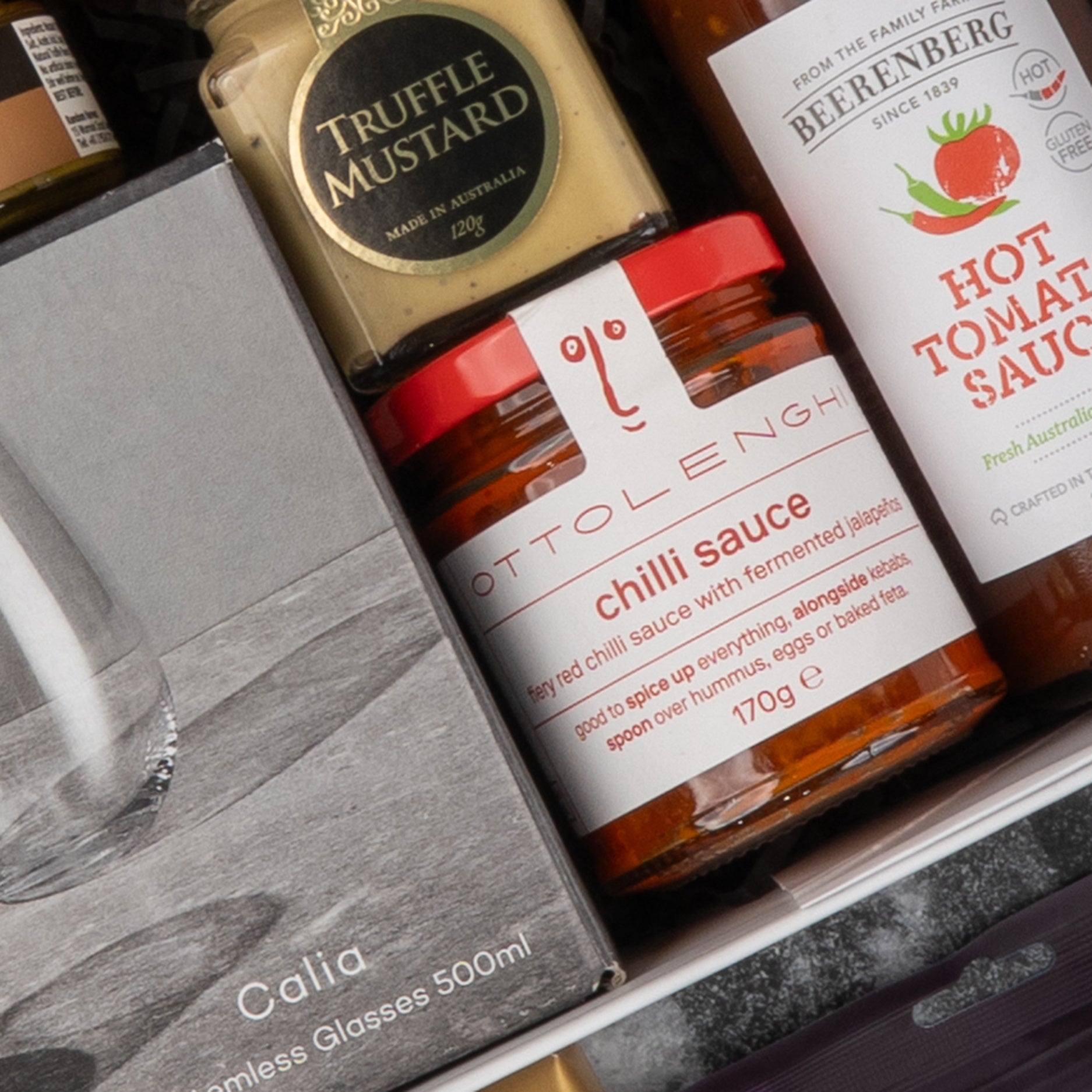 A close-up of The Hamper Boutique Co's Gourmet Collection Gift Hamper, featuring premium items like truffle mustard, Ottolenghi chilli sauce, and Berenberg hot tomato sauce elegantly arranged in a gift box.
