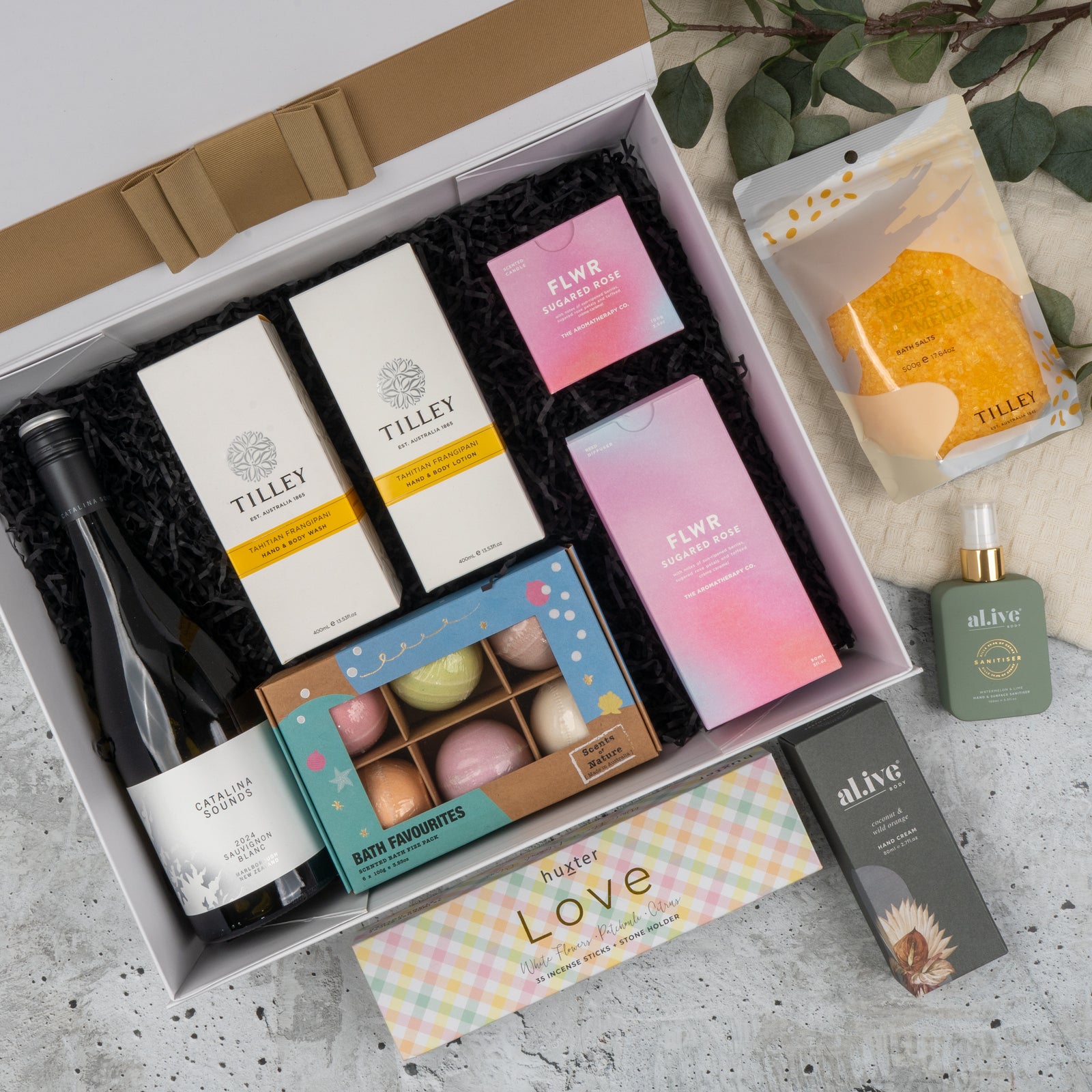 The Hamper Boutique Co's Ultimate Self-Care and Chardonnay Hamper features wine, Tilley soaps, FLWR bath and shower products, bath bombs, Alive skincare, and honeycomb, beautifully arranged on marble with greenery.