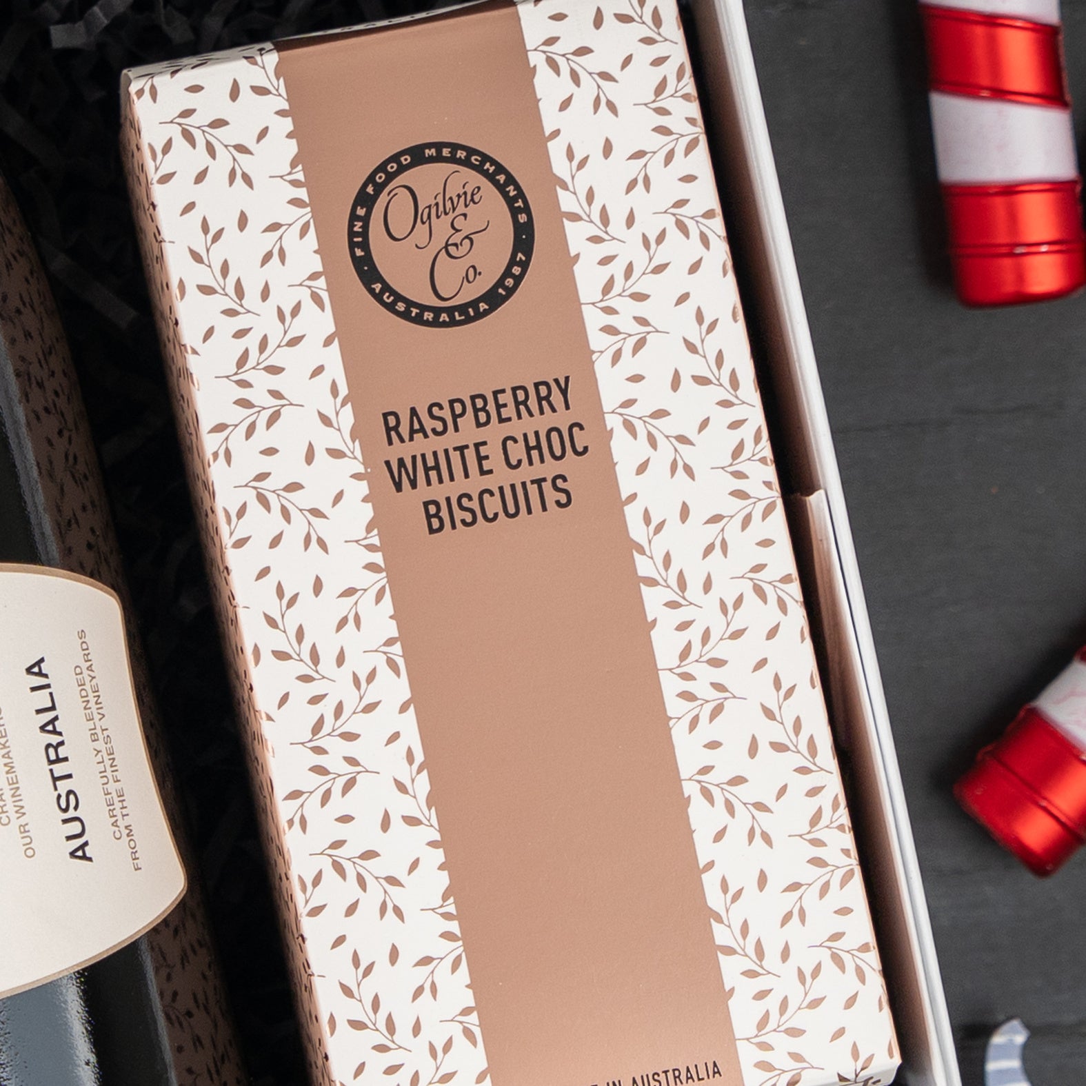 A Chandon Sparkling Gourmet Hamper by The Hamper Boutique Co, featuring a box of Ogilvie & Co. Raspberry White Choc Biscuits with a beige and white leaf pattern, surrounded by other assorted gift items.