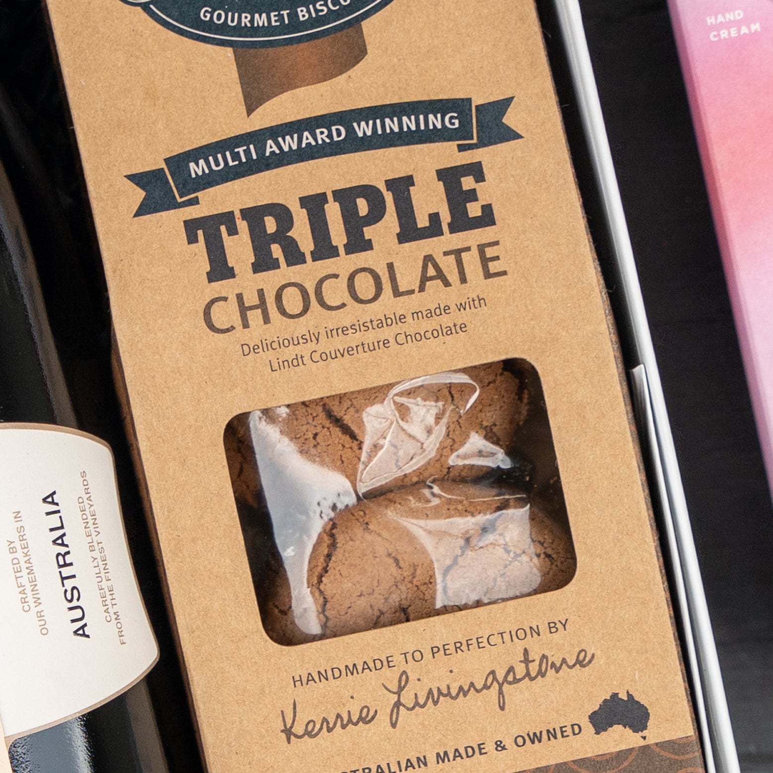 A Festive Fizz & Pamper box by The Hamper Boutique Co features a clear window displaying gourmet biscuits, with packaging noting they’re handmade by Kerrie Livingstone using Lindt chocolate.