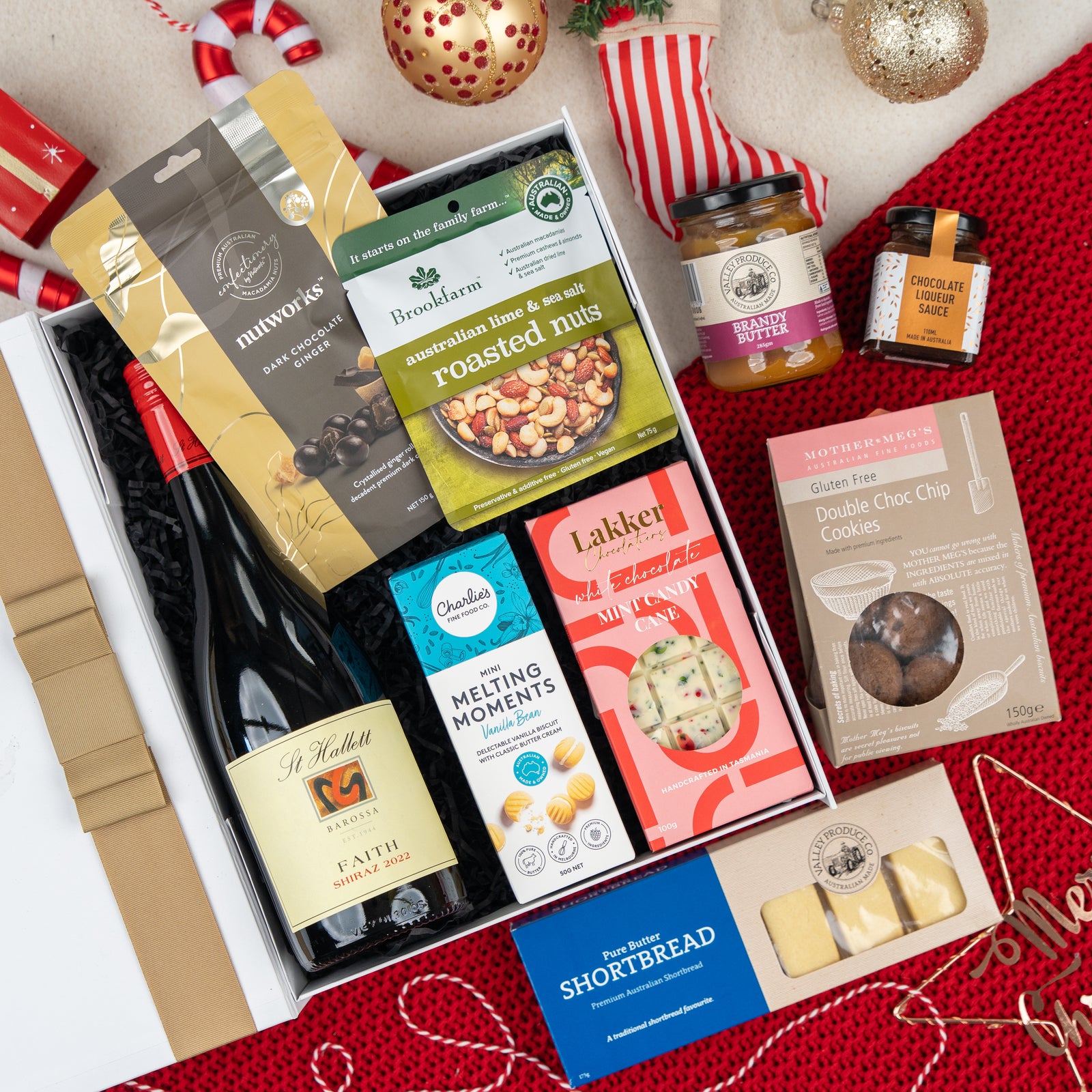 The Hamper Boutique Co’s Gourmet Gathering is a holiday gift box with red wine, roasted nuts, chocolate, shortbread, and jams, all beautifully packaged with festive decorations for a perfect seasonal treat.