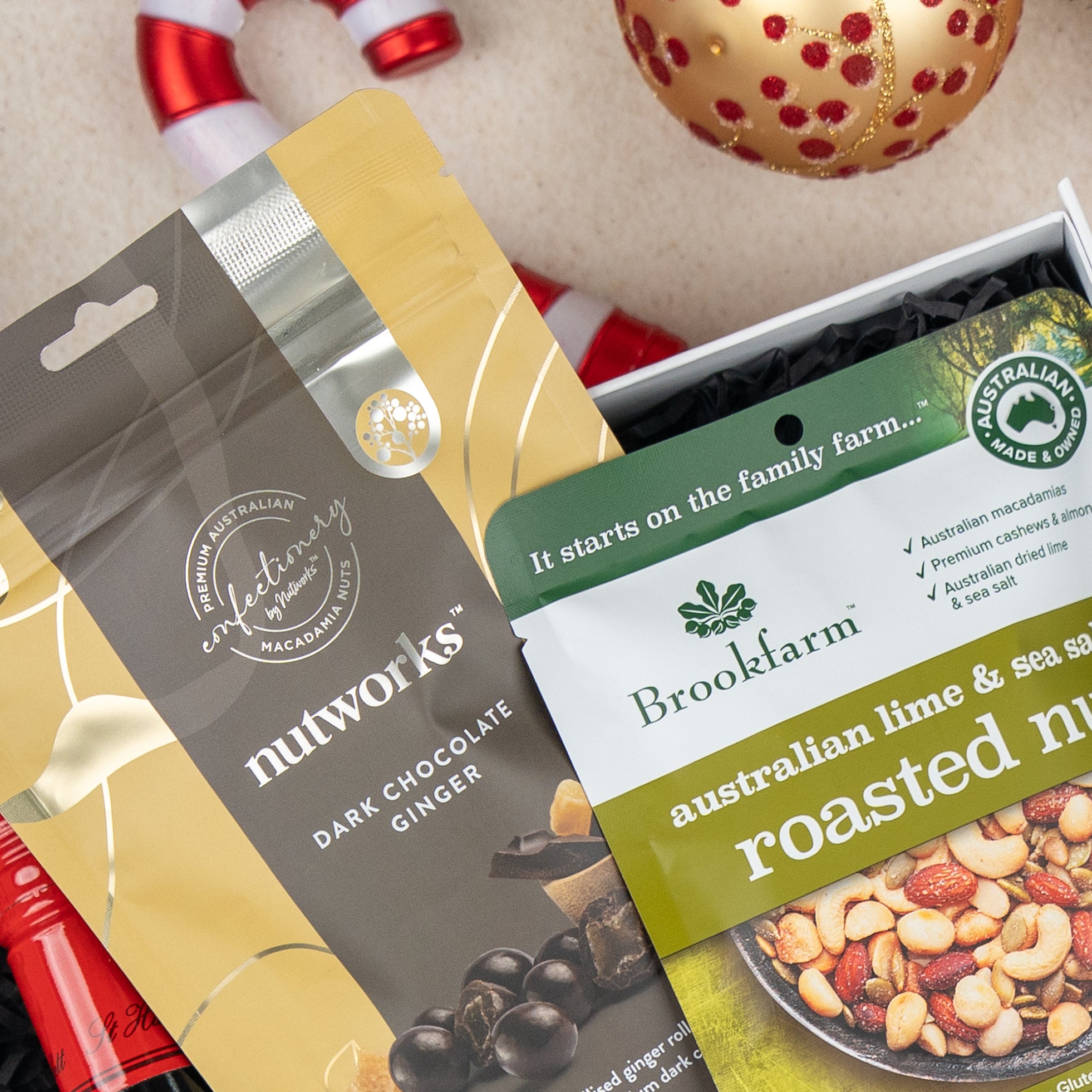 A close-up of festive snacks from The Hamper Boutique Co’s Gourmet Gathering, featuring chocolate ginger and lime roasted nuts, set on a textured surface with a candy cane and Christmas ornament nearby.