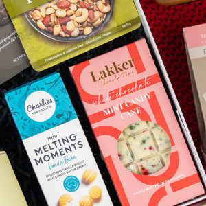 The Hamper Boutique Co's Gourmet Gathering box features assorted treats, like mixed nuts, a Charlies Mini Melting Moments Vanilla Bean biscuit box, and a Lakker Chocolatiers Mint Candy Cane white chocolate bar with candy pieces.