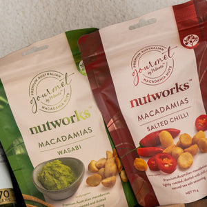 Two Gourmet Feast & Chardonnay snack bags from The Hamper Boutique Co are shown: one features a bowl of wasabi with nuts, the other shows red chilies and coated nuts on the packaging.