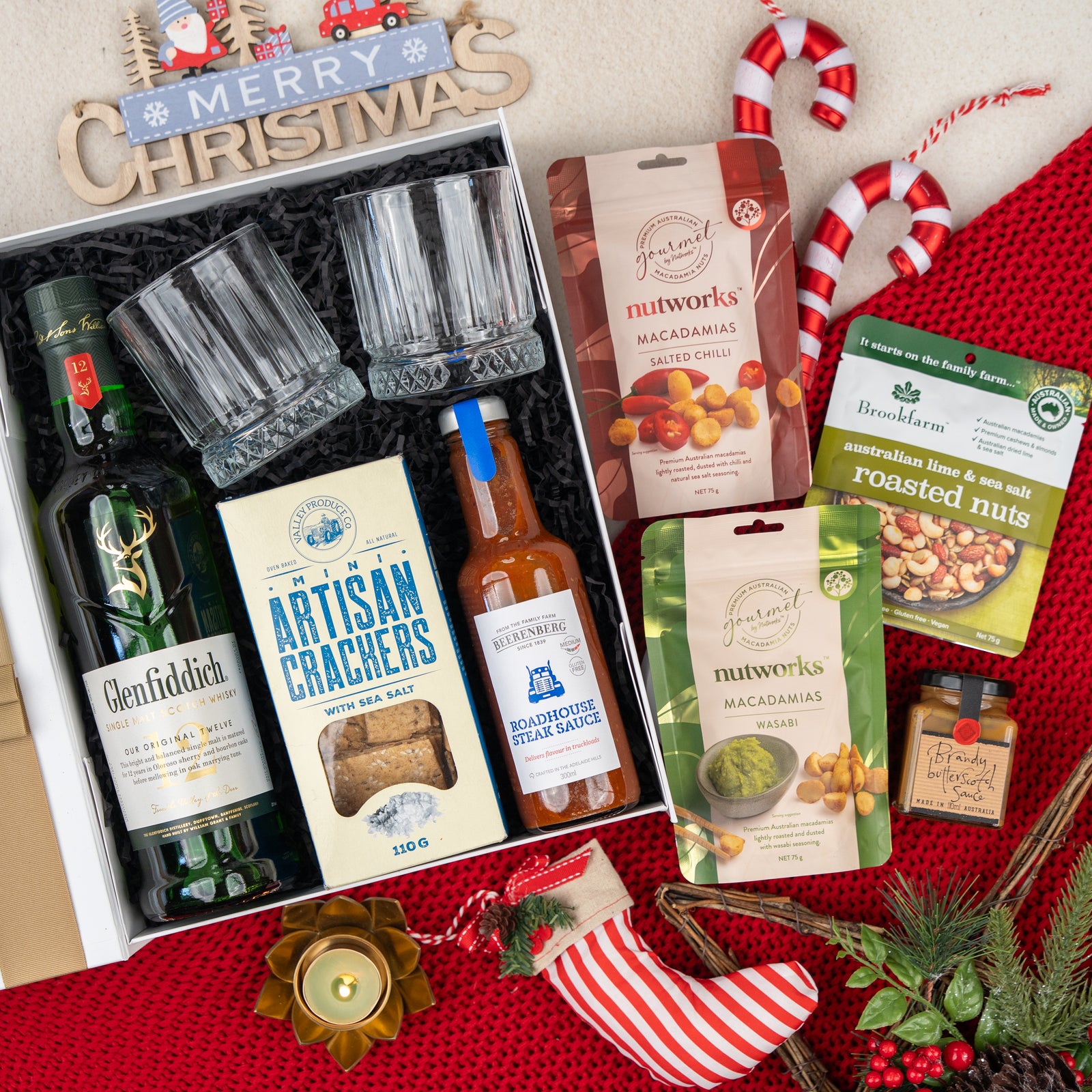 Whisky Wonder by The Hamper Boutique Co includes Glenfiddich whisky, two glass tumblers, artisan crackers, hot sauce, two nut packs, roasted nuts, candy canes, and festive decorations—all beautifully presented.