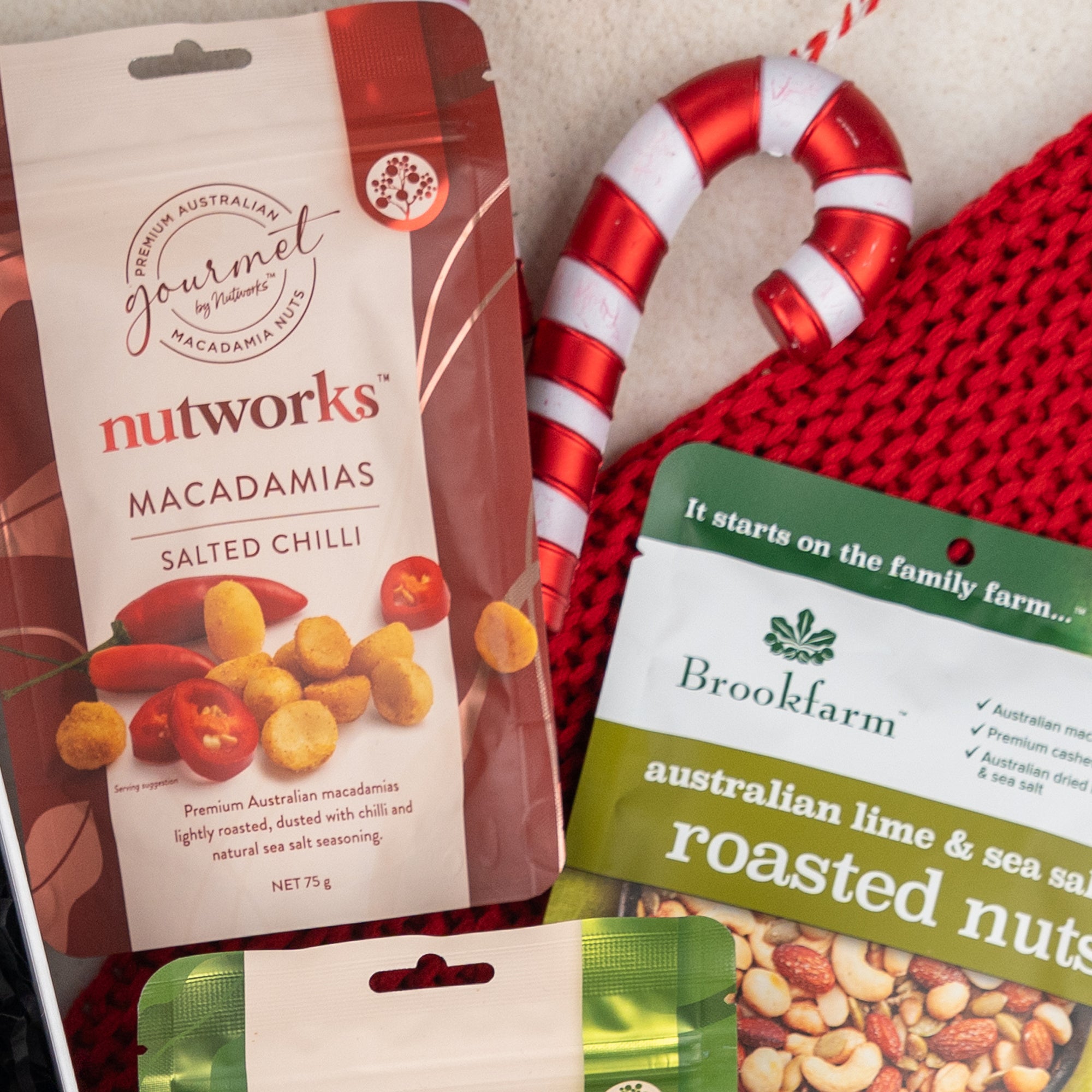 A festive Whisky Wonder arrangement by The Hamper Boutique Co featuring a red and white candy cane, red knit fabric, Nutworks salted chilli macadamias, and Brookfarm roasted nuts.