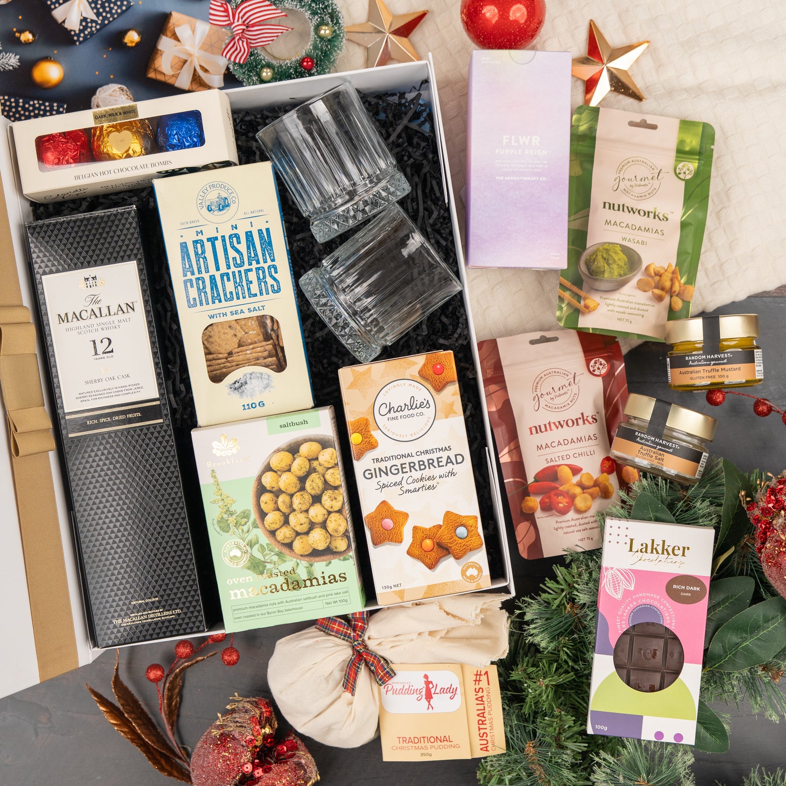 The Hamper Boutique Co's Whisky Celebration Extravaganza is a festive gift hamper with whisky, crackers, chocolates, gingerbread, macadamias, jam, panettone, tea, and holiday decorations arranged beautifully for celebration.
