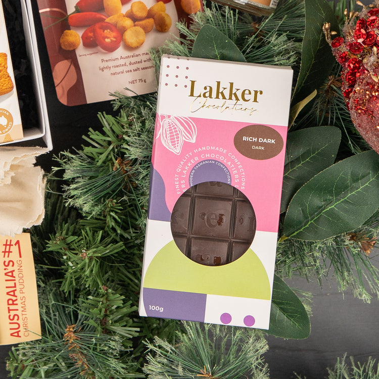 A box of The Hamper Boutique Co Whisky Celebration Extravaganza is displayed on festive green pine branches, with other holiday treats partly visible nearby.