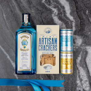 The Hamper Boutique Co’s Bombay Sapphire Gin and Tonic Hamper is displayed on a gray marble surface with a blue ribbon in the corner.