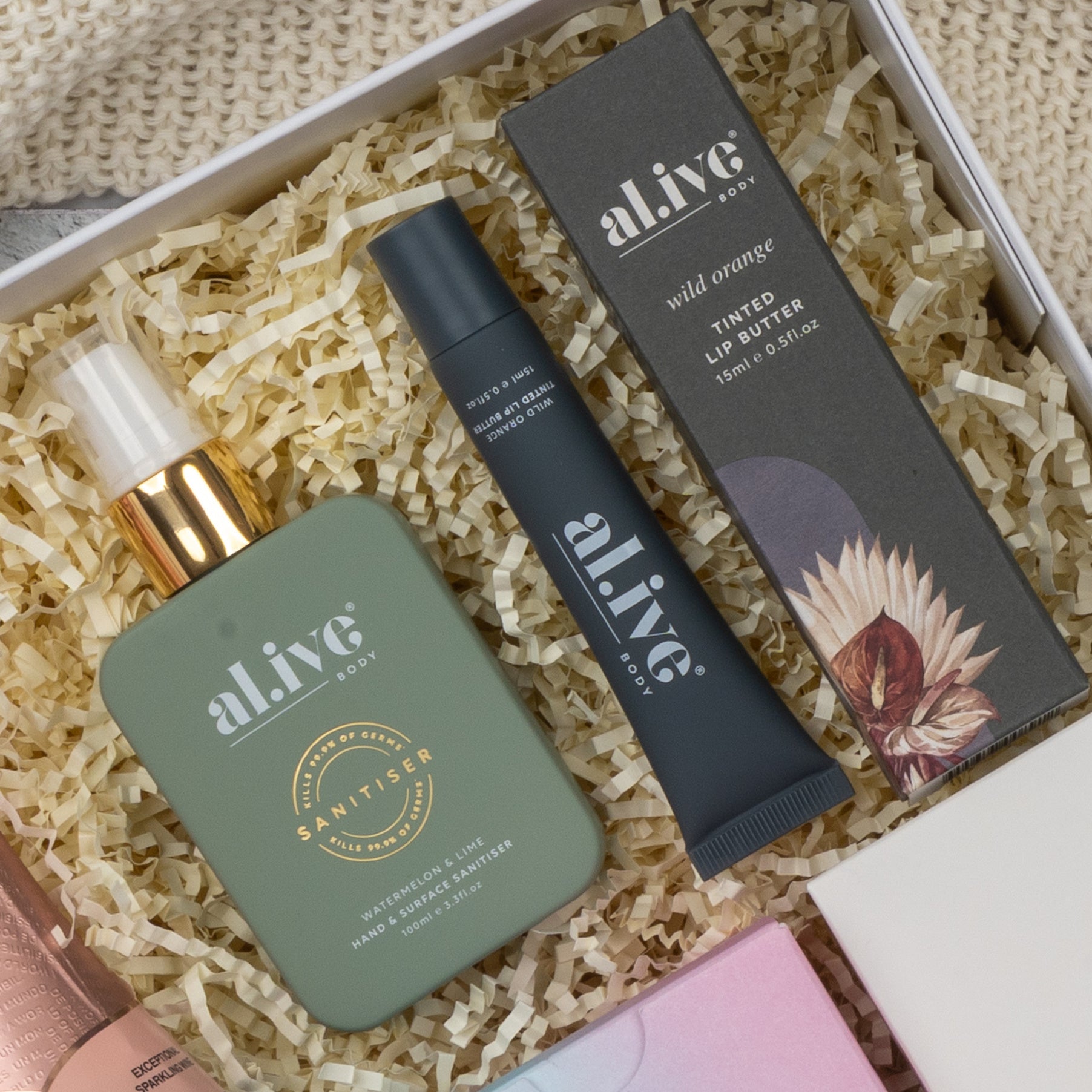 The Hamper Boutique Co's Chandon Rosé Pamper Hamper features Alive Body hand sanitizer and Wild Orange Tinted Lip Butter in a gift box with shredded paper, plus glimpses of additional products.