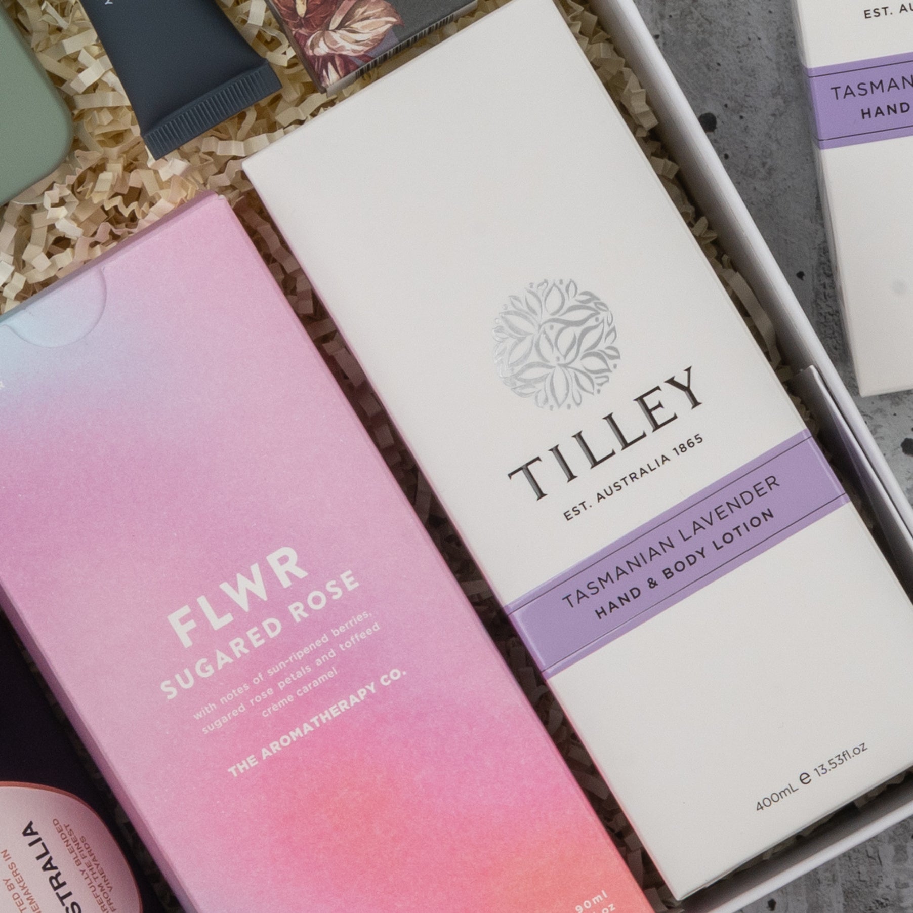 The Chandon Rosé Pamper Hamper by The Hamper Boutique Co features skincare products in a stylish gift box, including a pink FLWR Sugared Rose and a white Tilley Tasmanian Lavender Hand & Body Lotion, nestled in shredded packing material.