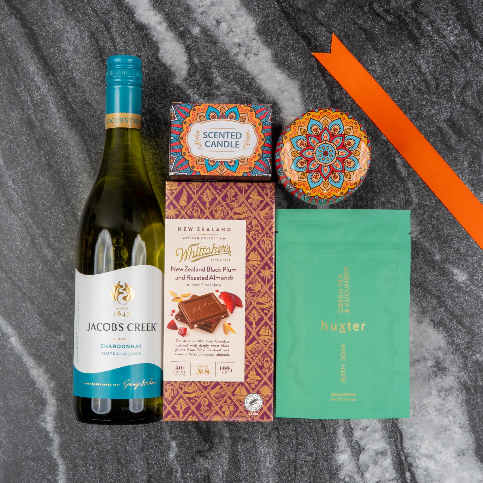 The Hamper Boutique Co’s Wine and Candlelight Hamper, featuring wine, a candle, chocolate, soap pouch, and a decorative tin, is displayed on gray marble with an orange ribbon.